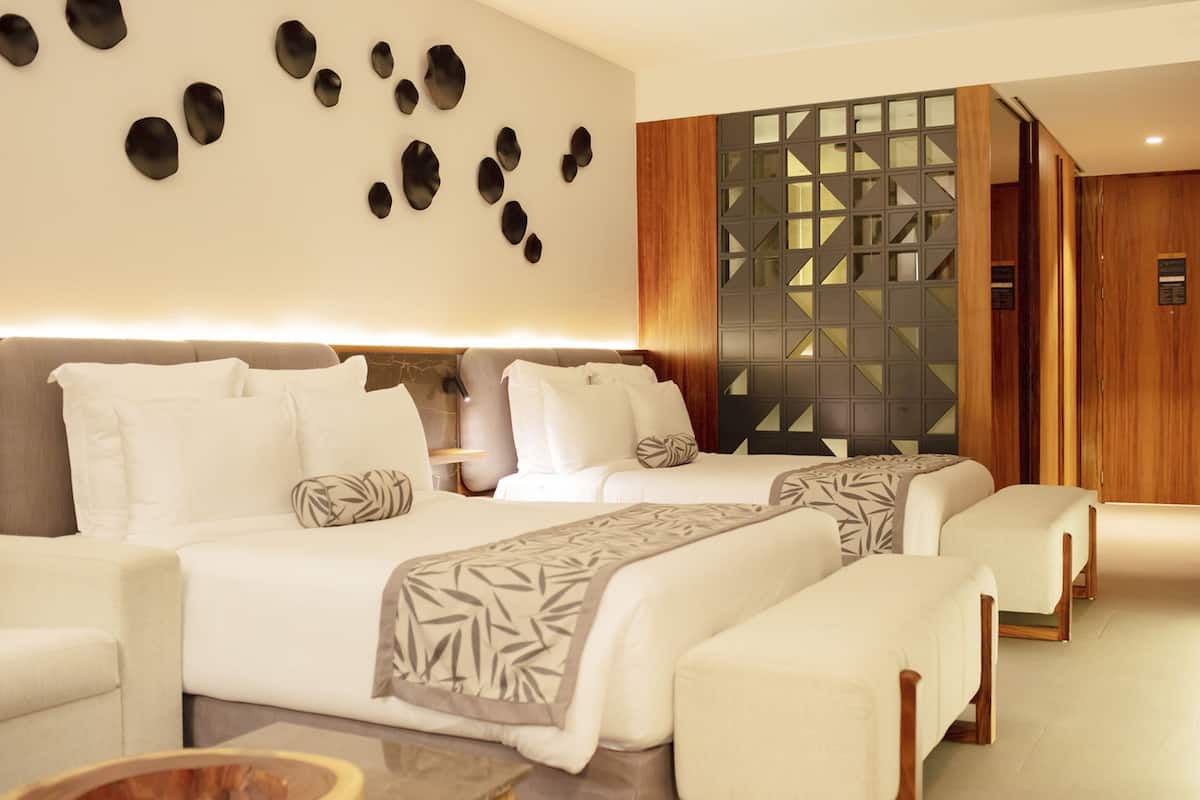 Habitación de hotel con dos camas, un sofá, una mesita de centro y una pared decorativa con diseños geométricos.
