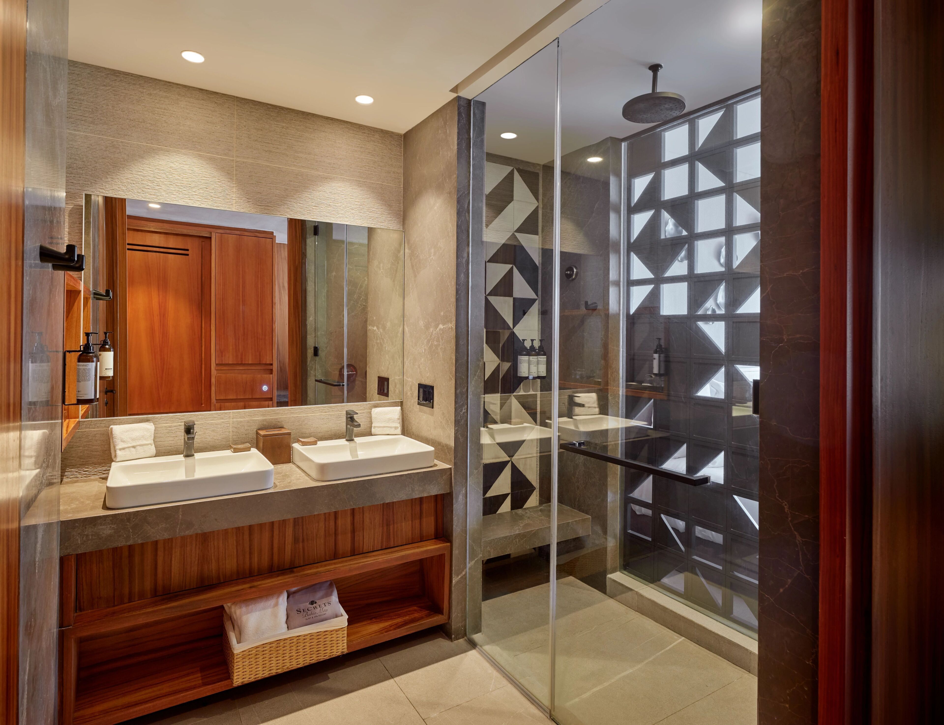 A modern bathroom with a wooden vanity, dual sinks, a glass shower enclosure, and a large mirror.