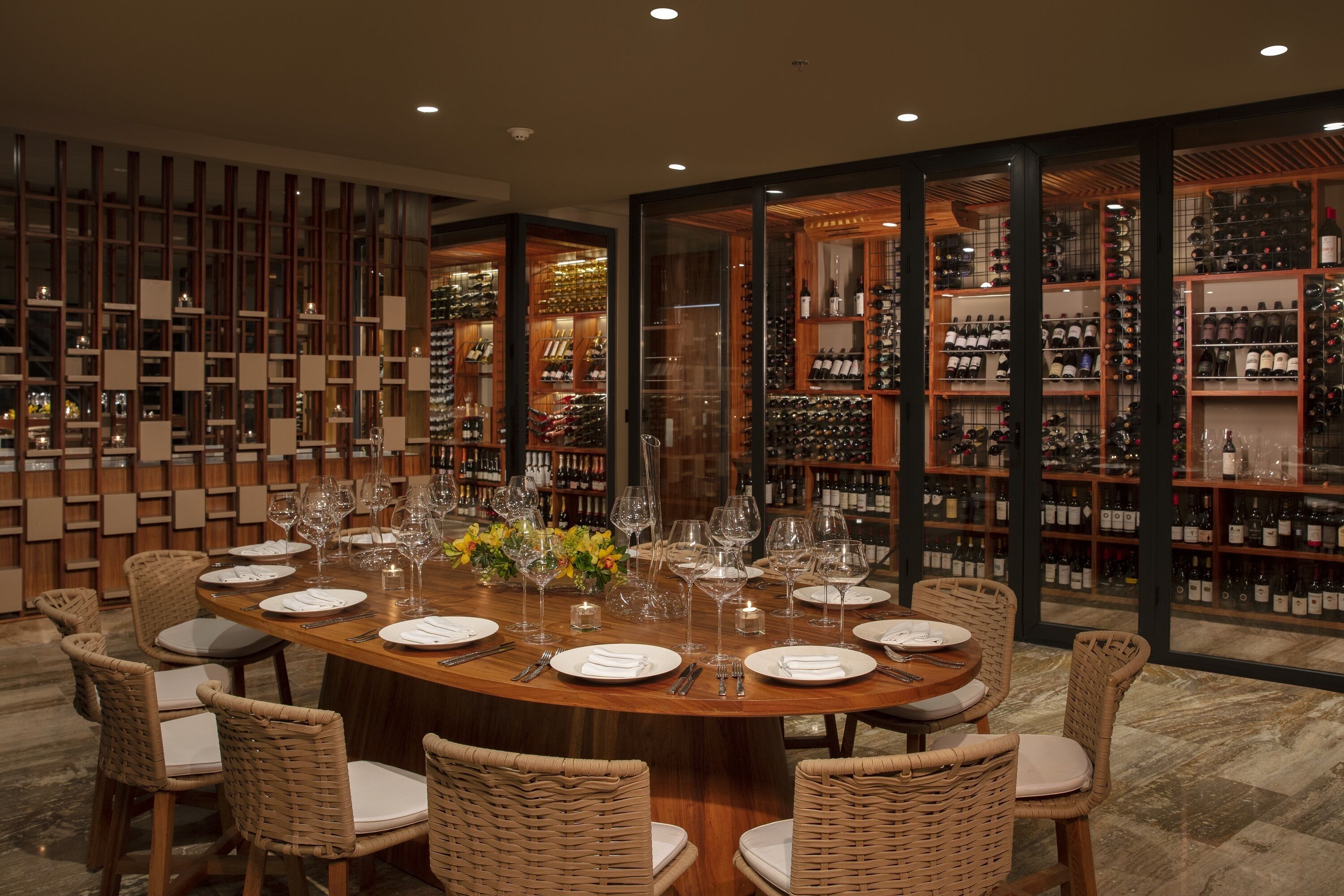 A dining area with a round table set for eight, surrounded by wicker chairs.