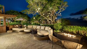 An outdoor seating area with a cushioned sofa, wicker chairs, and a fire feature.