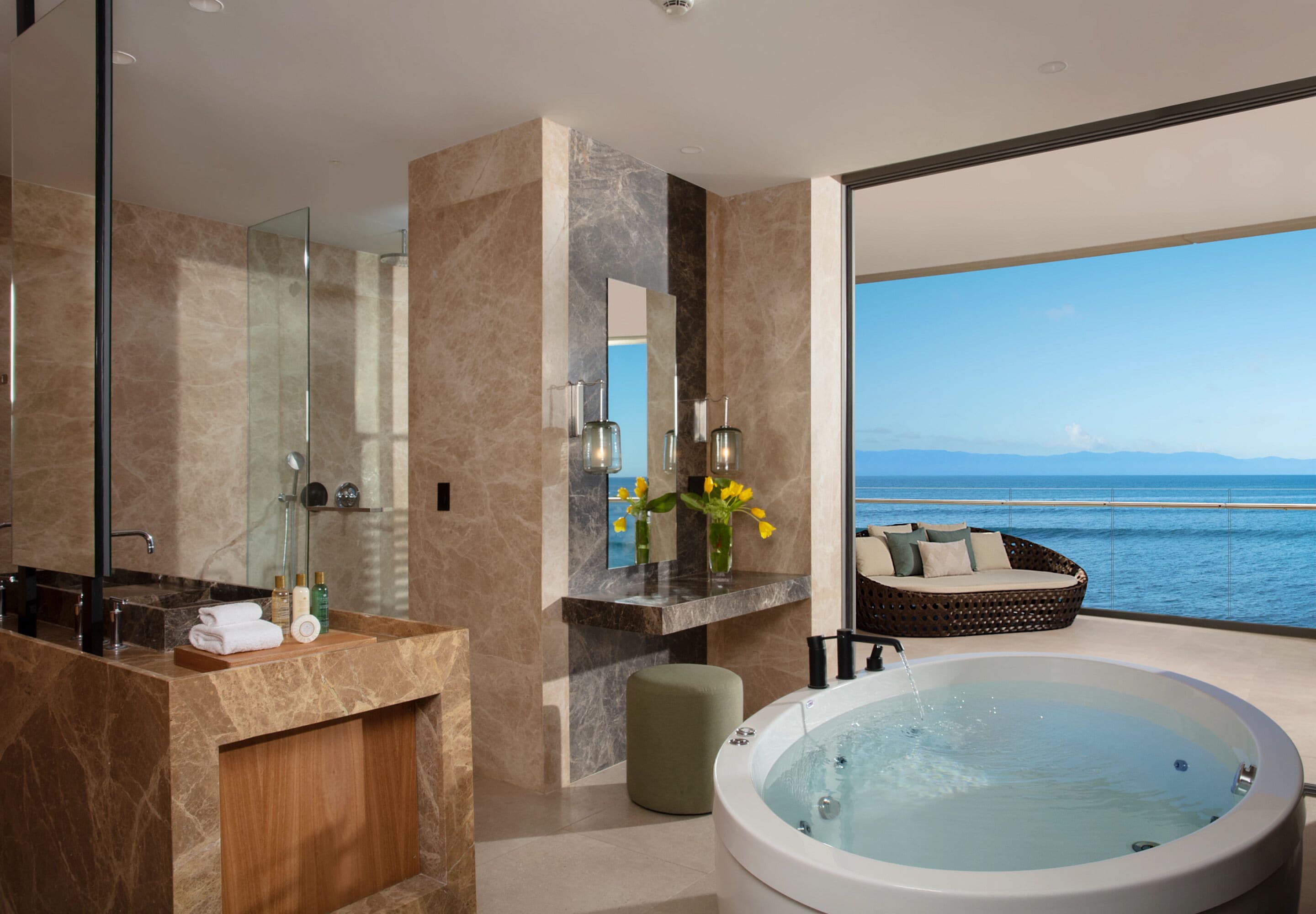 Un baño moderno con una bañera grande, un tocador con espejo y vista al océano.