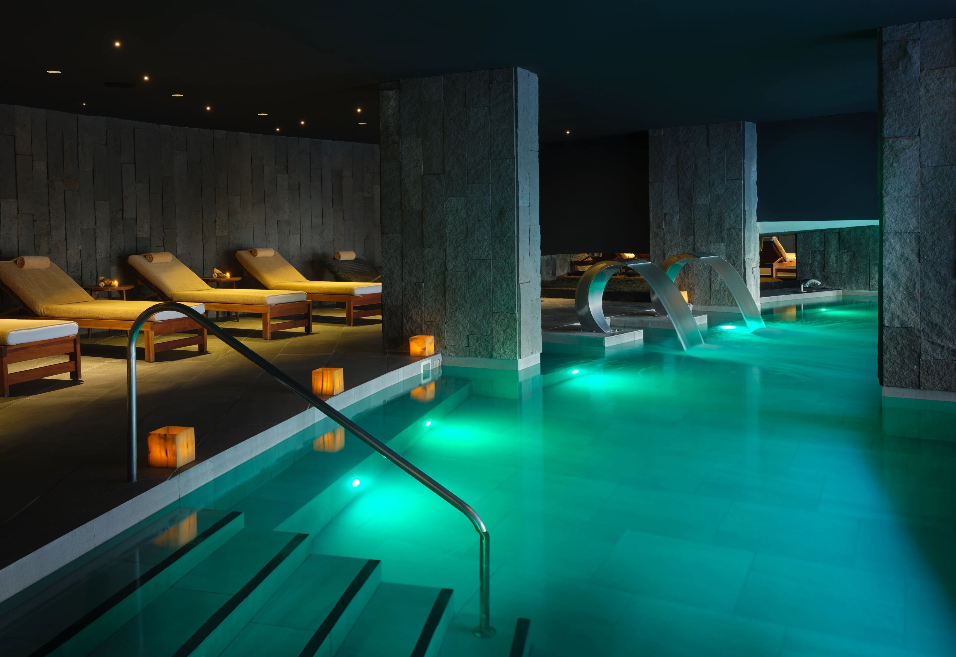 Ein Wellnessbereich mit Pool, Liegestühlen und einer Steinwand.