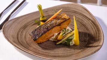 A plate with a piece of salmon, vegetables, and a decorative garnish.