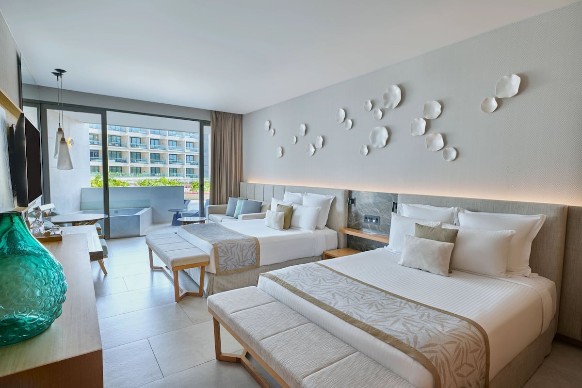 Habitación de hotel moderna con dos camas, un sofá, una zona de comedor y un amplio ventanal con vistas a la ciudad.