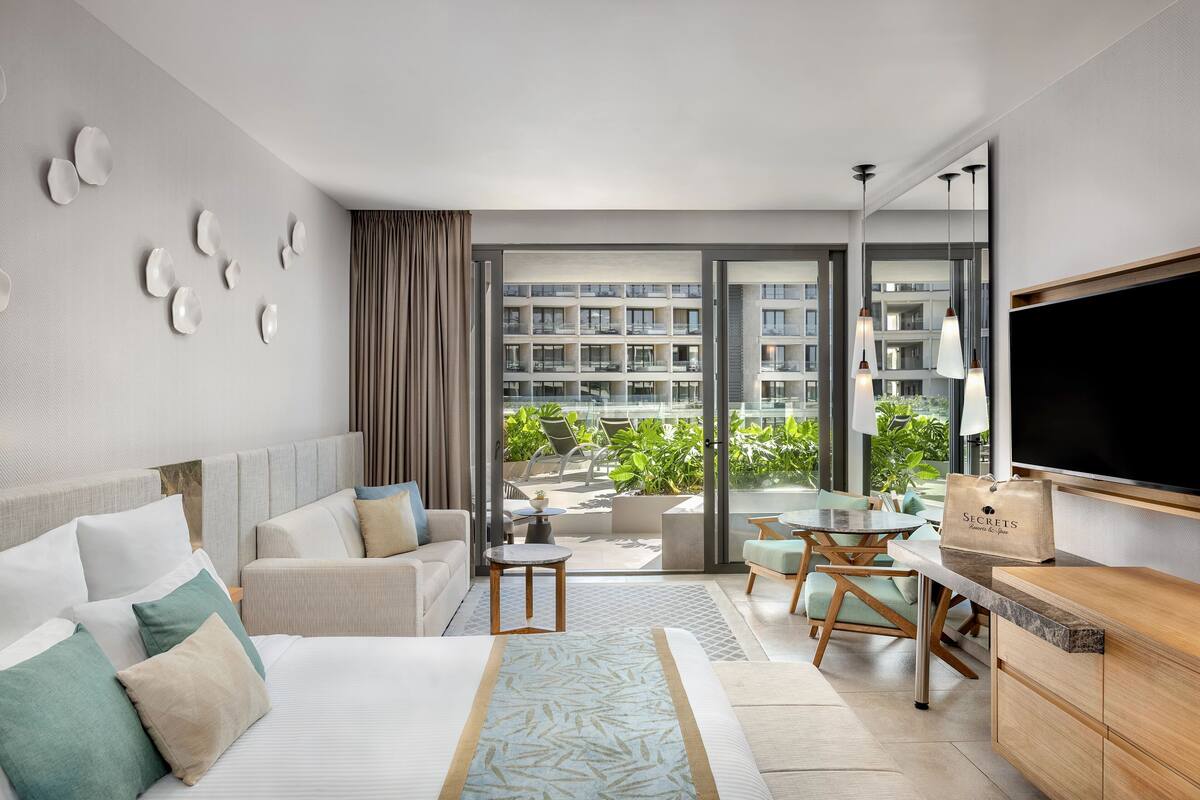 Una habitación de hotel moderna con cama, sofá, zona de comedor y televisión.