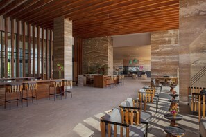 A spacious lobby with a wooden ceiling, a bar area with stools, and a seating area with tables and chairs.
