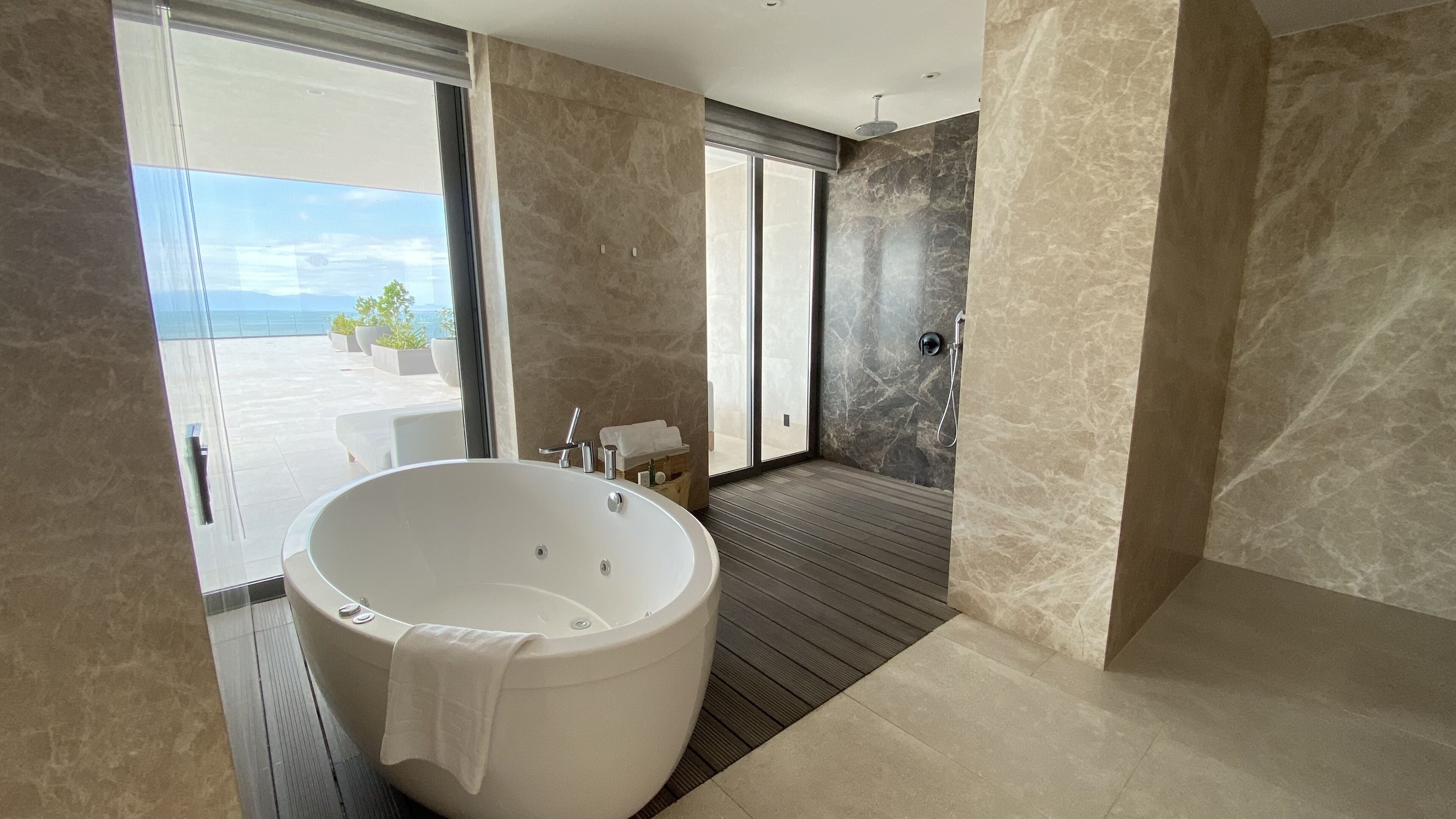 Un baño moderno con una bañera independiente grande, cabina de ducha con mampara de cristal y vistas a la terraza exterior.