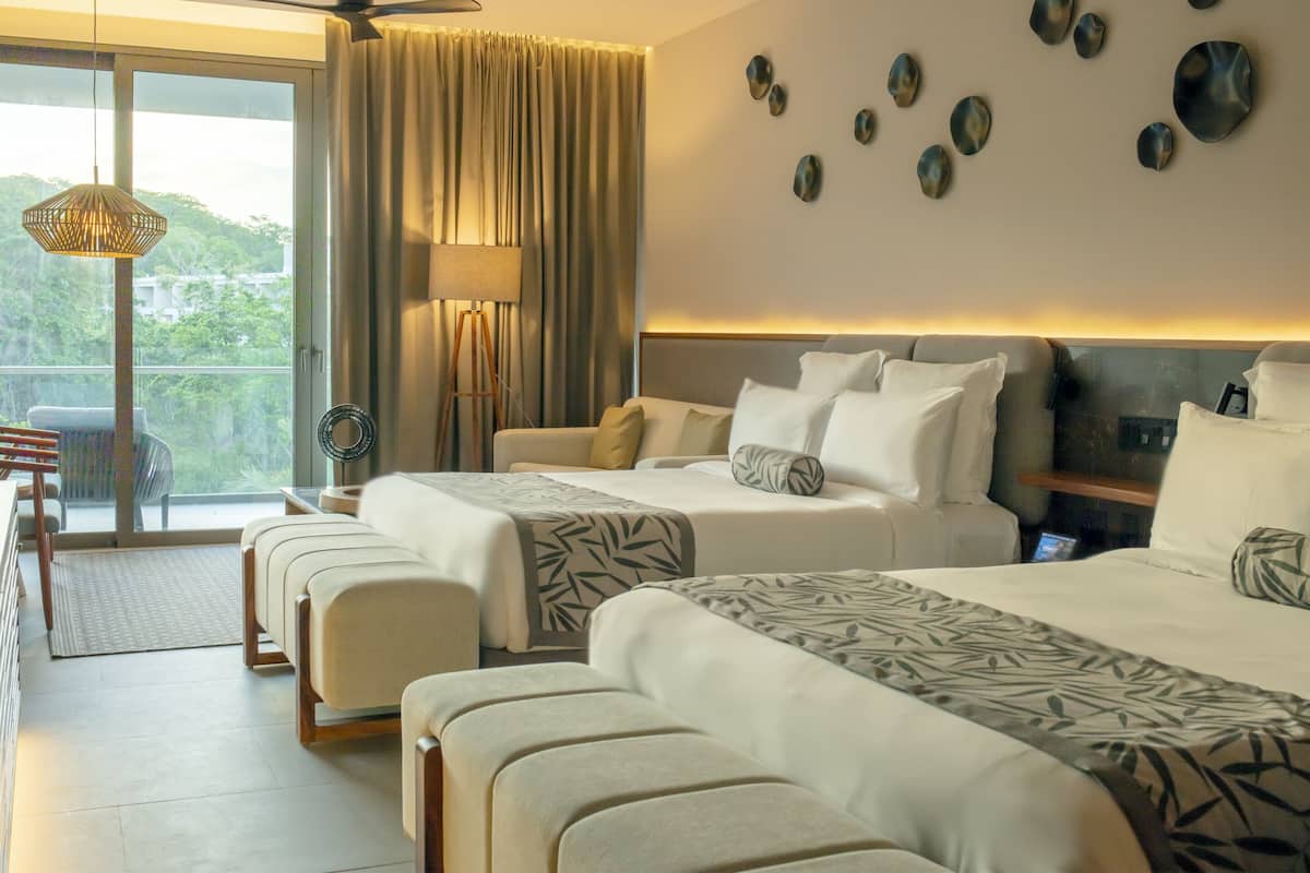 Habitación de hotel con balcón, cama con colcha estampada, lámpara de pie y pared decorada con platos.