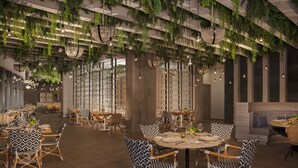 A restaurant with round tables, patterned chairs, hanging plants, and pendant lighting.