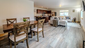 Un amplio salón con una mesa de comedor de madera, sillas, un sofá y una cocina al fondo.