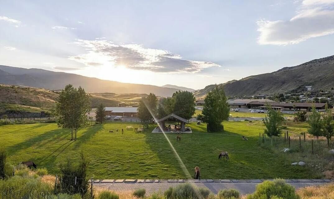 Paisagem rural com um coreto, campos abertos e colinas ao longe.