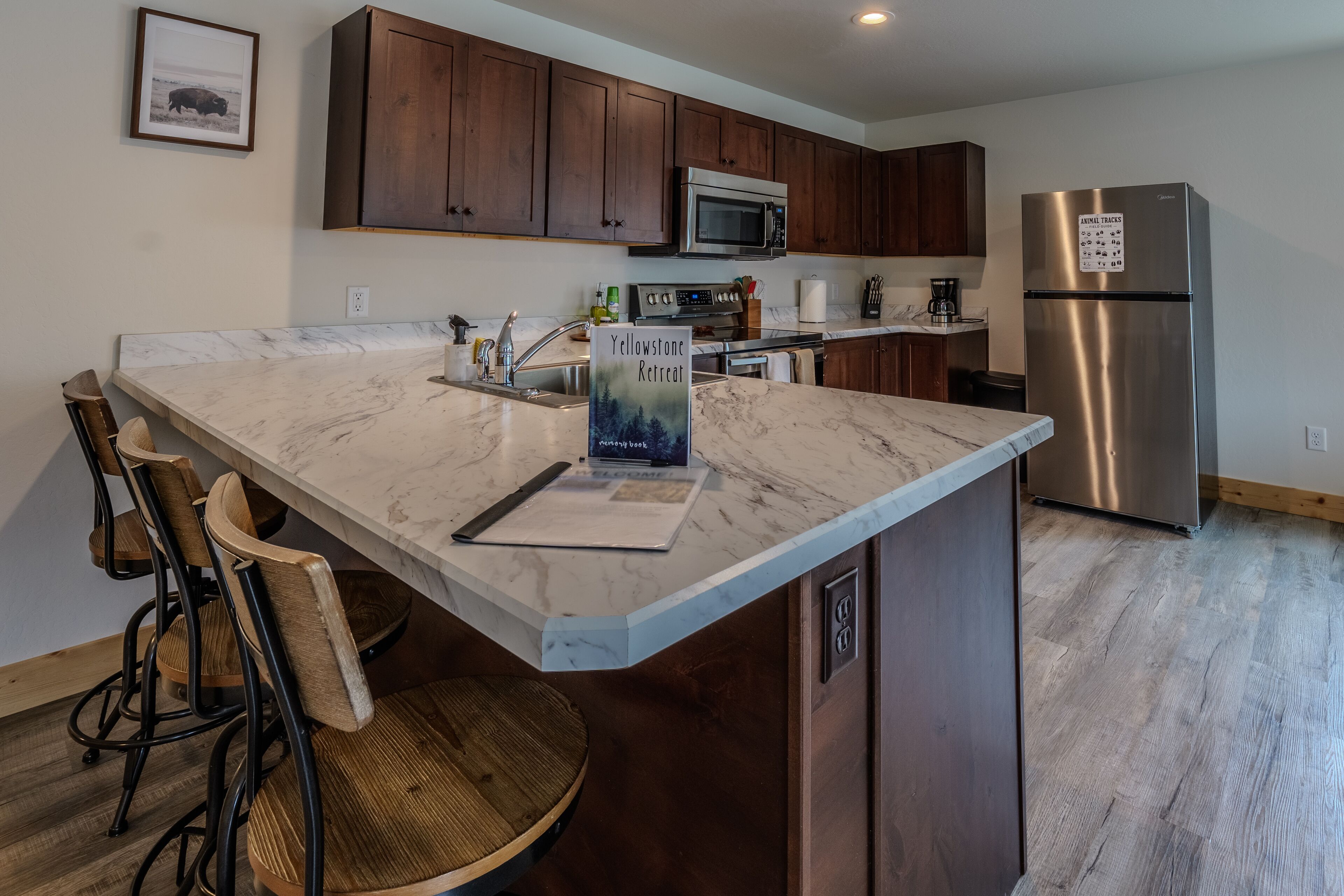 Una cocina con encimeras de mármol, sillas de madera, un refrigerador de acero inoxidable y un letrero que dice "Yellowstone Retreat".