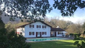 Une maison blanche avec une piscine, entourée de verdure et d’arbres.