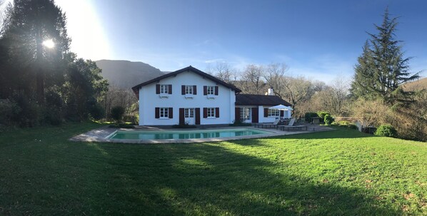 Une maison à deux étages avec une piscine, entourée d’une pelouse bien entretenue et d’arbres.