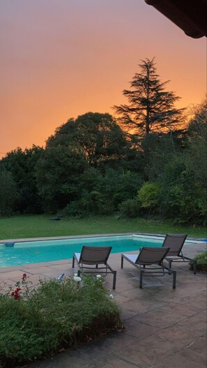 Un espace aménagé au bord de la piscine, avec des chaises longues et une vue sur le coucher de soleil.
