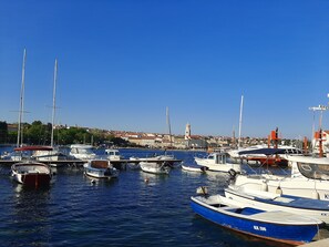 Un port de plaisance où sont amarrés différents types de bateaux, un ciel bleu azur et une ville en arrière-plan.