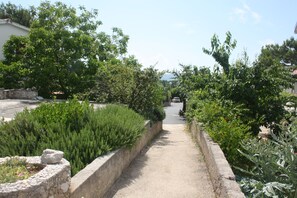 Un sentier bordé d’une végétation luxuriante et de murs de pierre, qui mène à un bâtiment situé au loin.