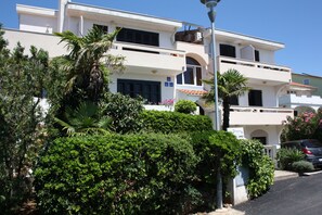Un immeuble à plusieurs étages doté de balcons, entouré d’une végétation luxuriante et surplombant un ciel d’un bleu limpide.