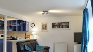 Un espace de vie compact comprenant un coin cuisine, un canapé, un téléviseur et un panneau décoratif encadré accroché au mur.