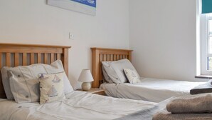 Une chambre avec deux lits simples, une table de chevet avec une lampe, un tableau représentant un ciel et des nuages, et une fenêtre donnant sur un paysage.