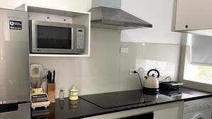 A modern kitchen with a stainless steel refrigerator, a microwave, a kettle, and a washing machine.