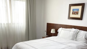 A neatly made bed with a wooden headboard, a bedside table with a lamp, and a framed picture on the wall.