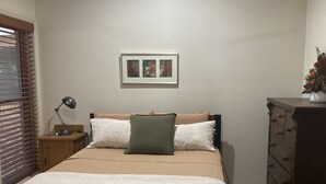 Una camera da letto con un letto, un comodino, una cassettiera, una ventola a soffitto e un quadro appeso al muro.