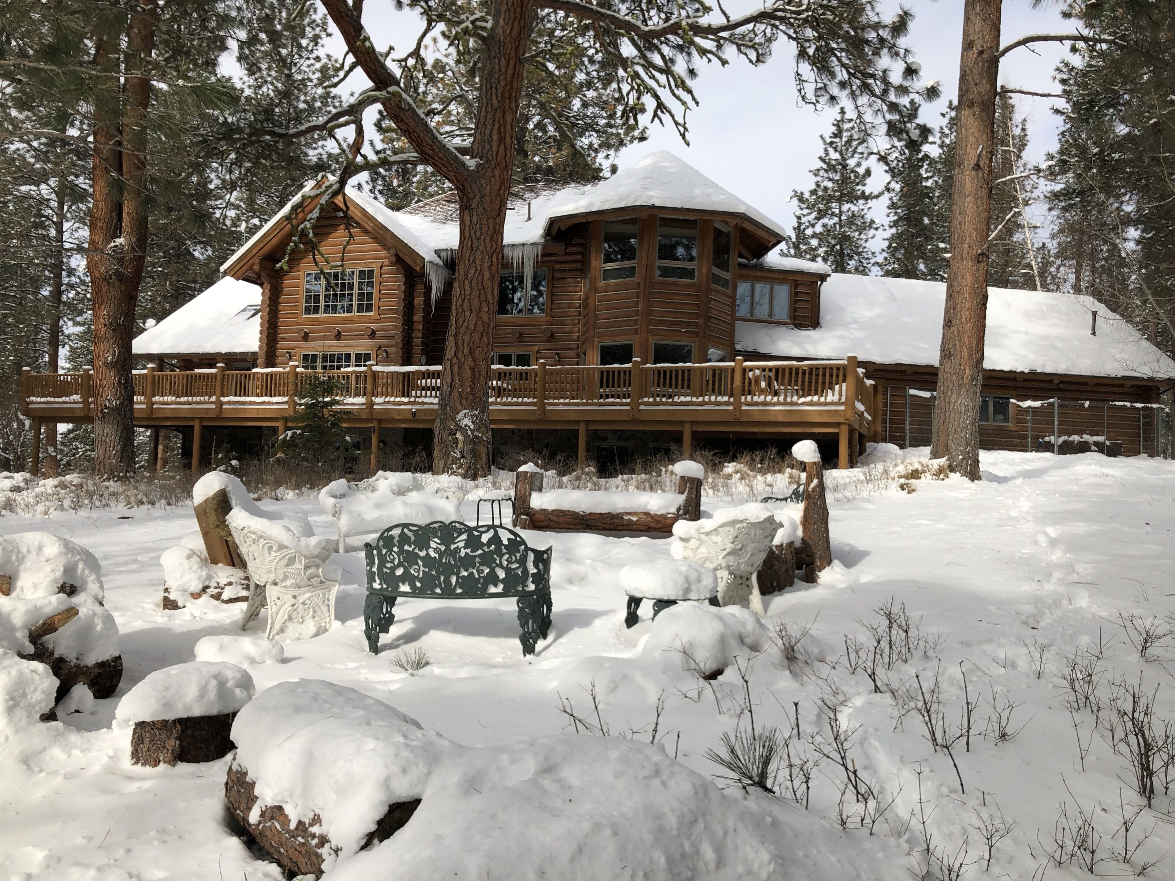 A large log cabin with a wooden deck and snow-covered roof.