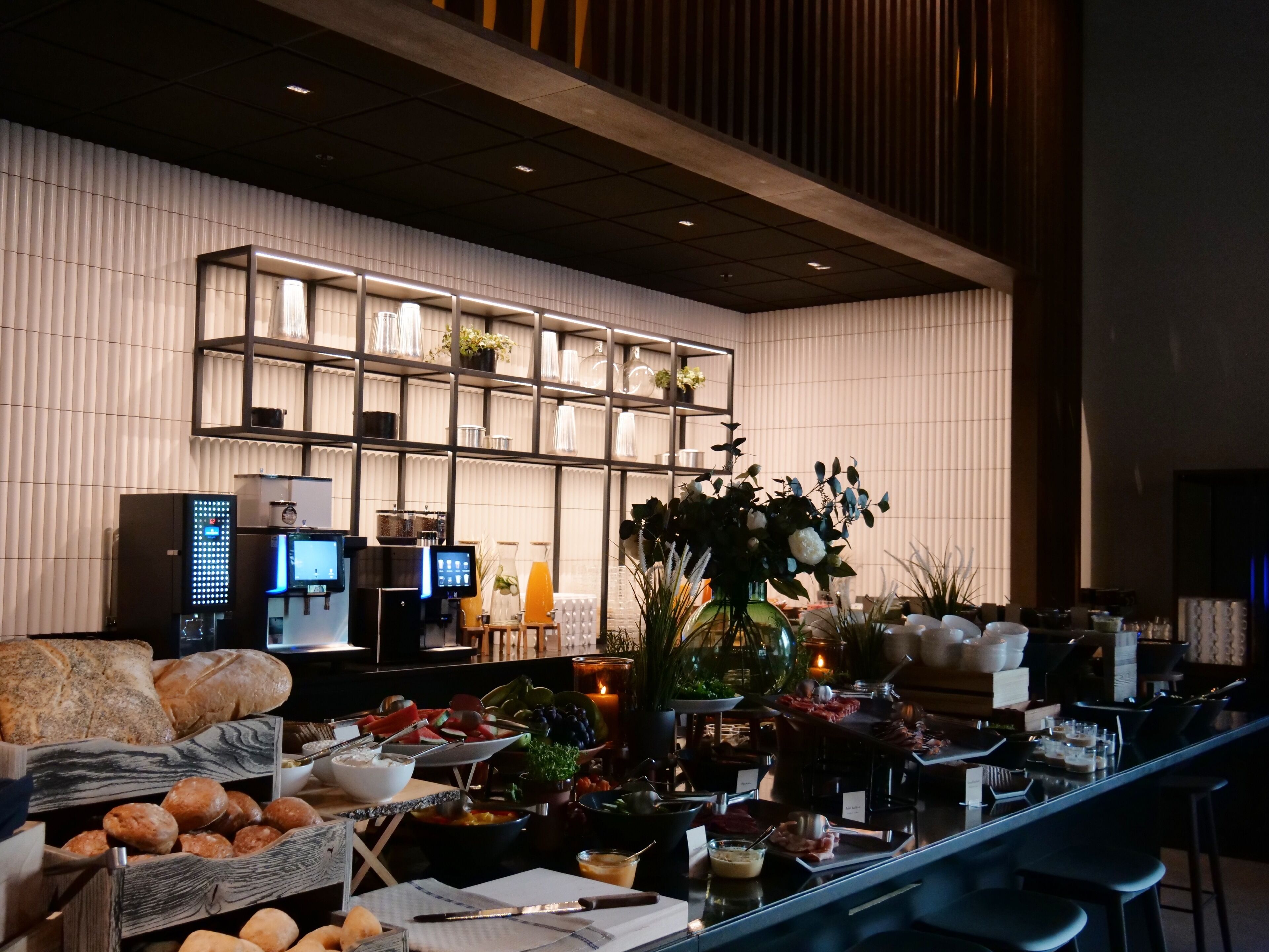 A modern hotel lobby with a buffet area, a reception desk, and a seating area with a large vase of flowers.