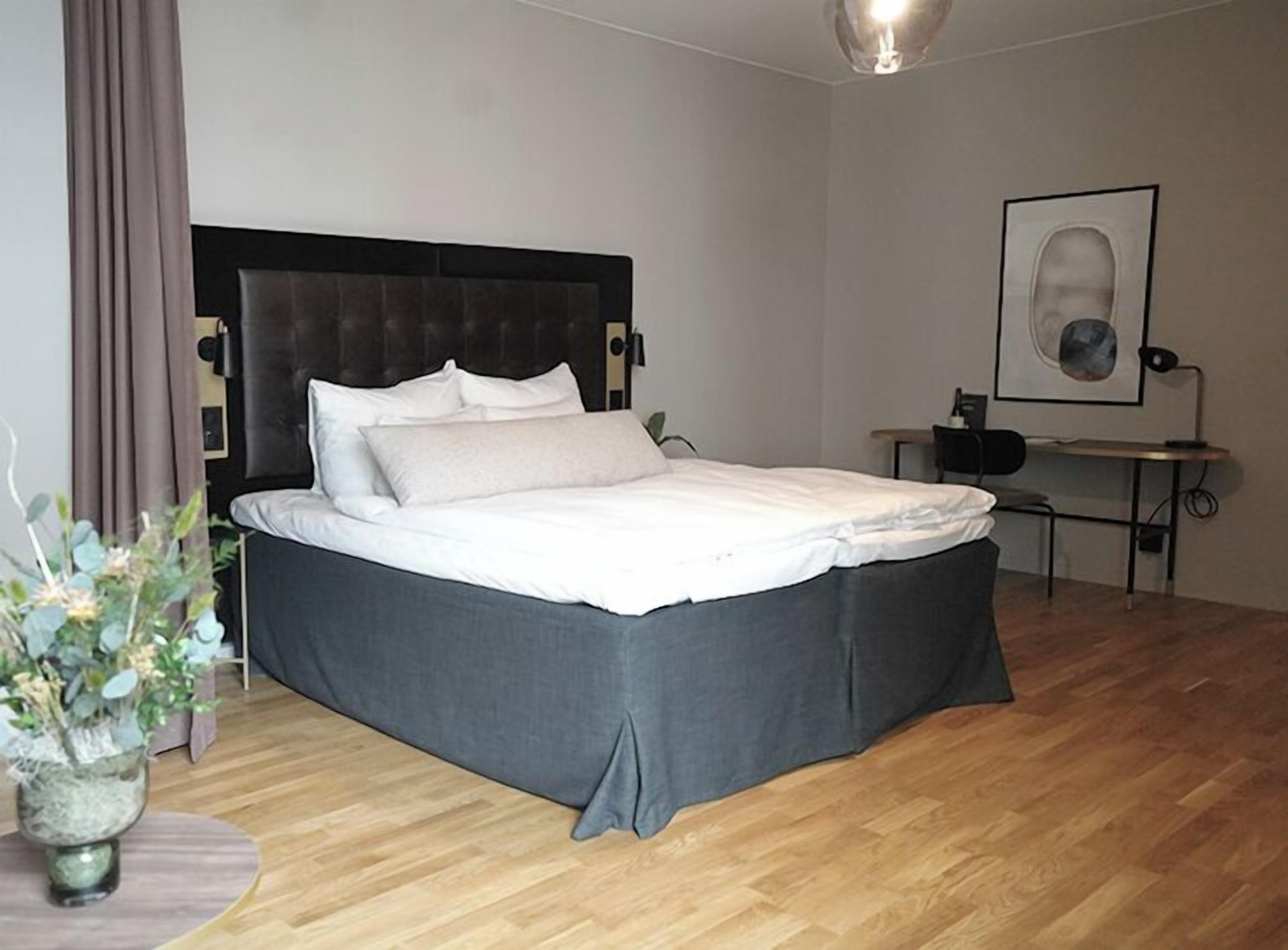A neatly made bed with white linens and a dark headboard in a room with wooden flooring.