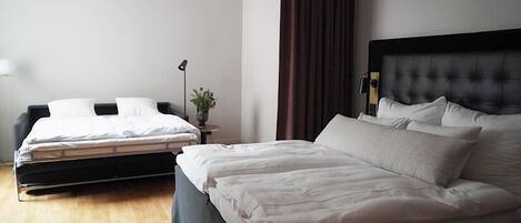 Una habitación de hotel con una cama grande, una cama más pequeña, una mesita de noche con lámpara y una planta.