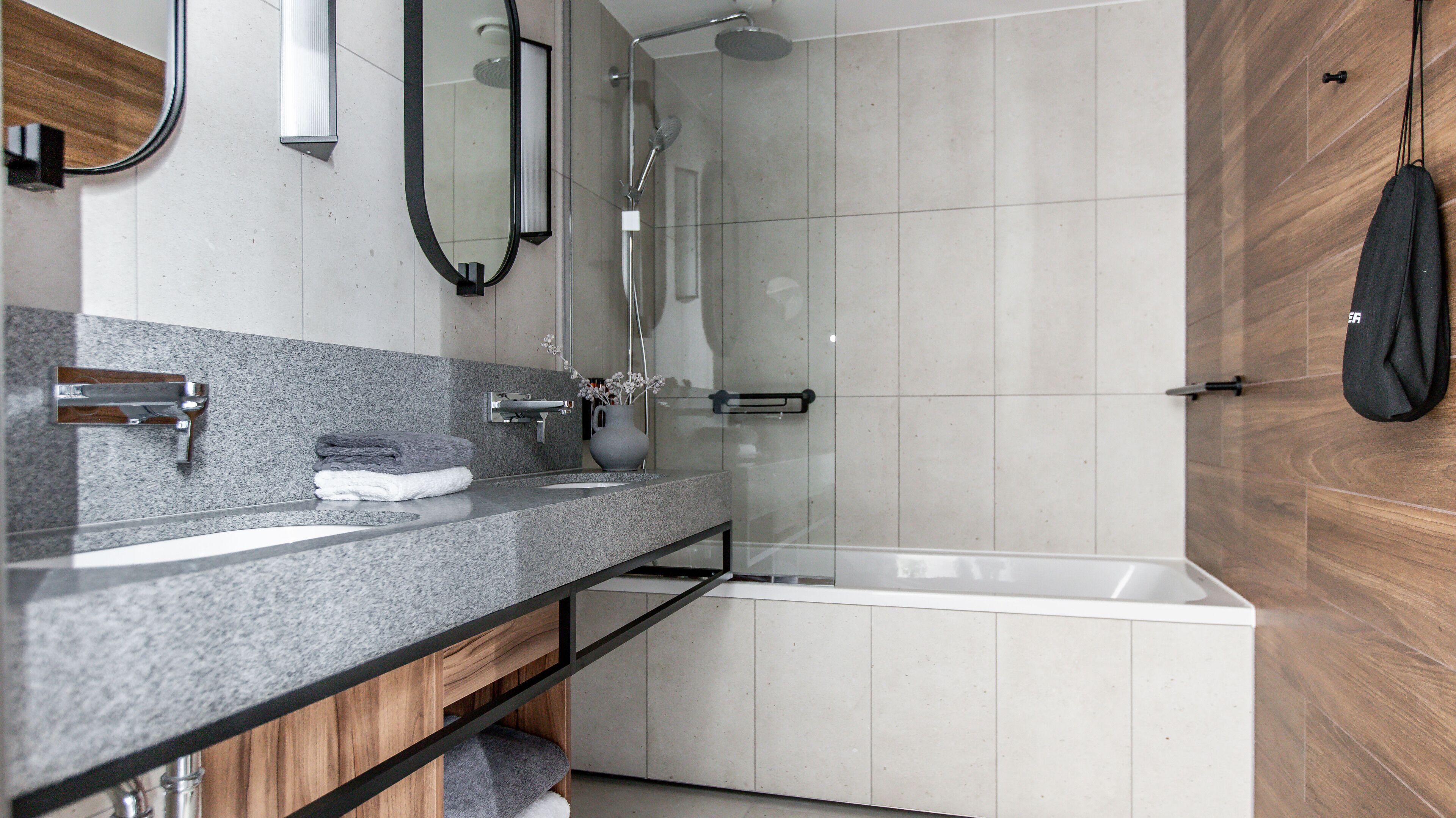 Un baño moderno con encimera de granito, un espejo, toallero, ducha y mueble de tocador de madera.