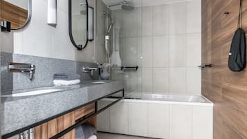 Un baño moderno con encimera de granito, un espejo, toallero, ducha y mueble de tocador de madera.
