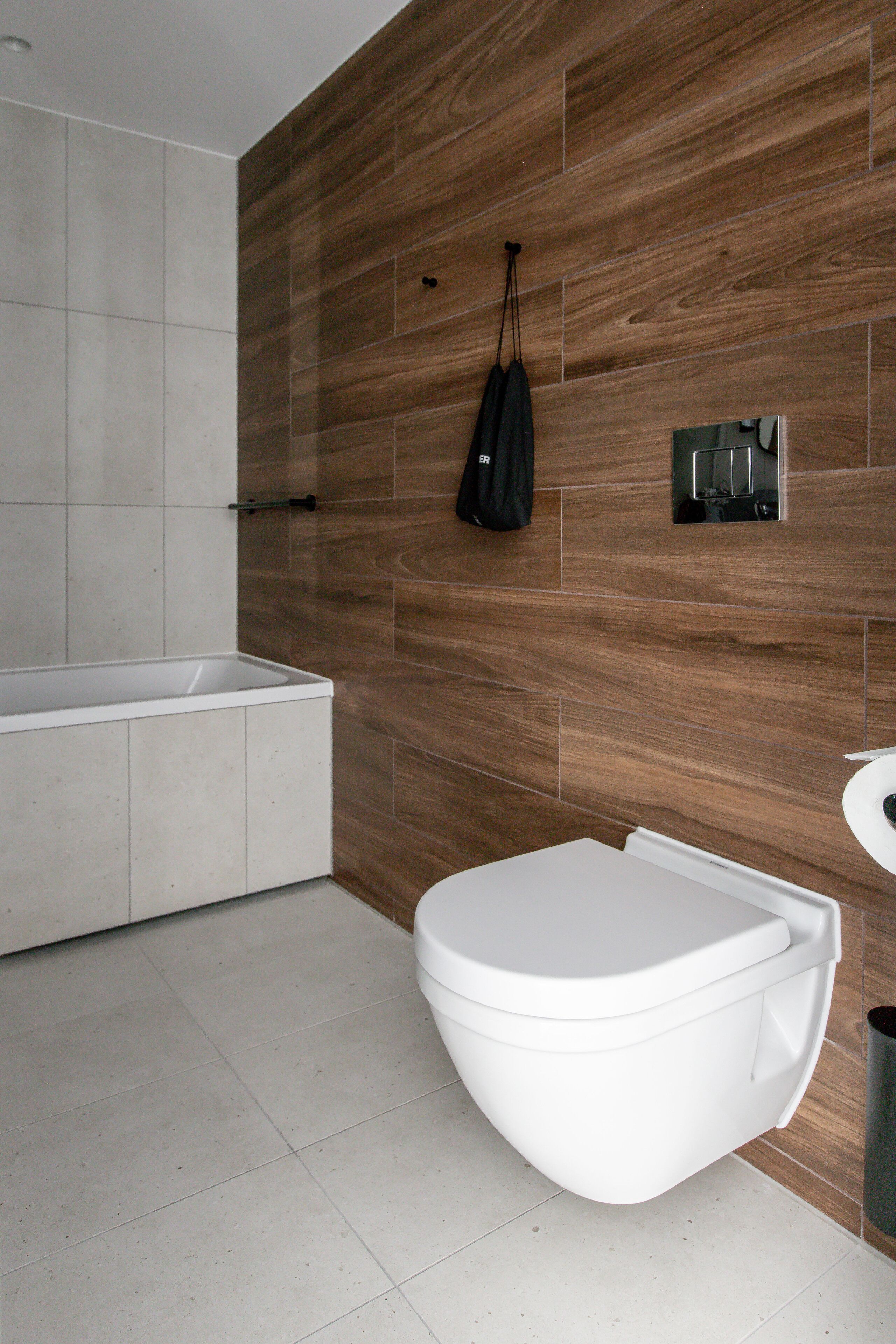 Un baño moderno con una bañera blanca, un inodoro blanco y una pared de madera.