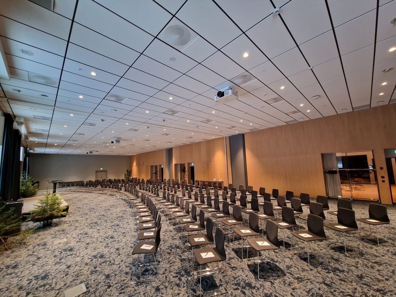 Une grande salle de conférence avec des rangées de chaises, une scène et un sol recouvert de moquette.