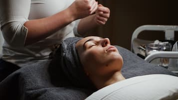 A person lying on a bed with a headband, another person attending to them, and a medical device in the background.
