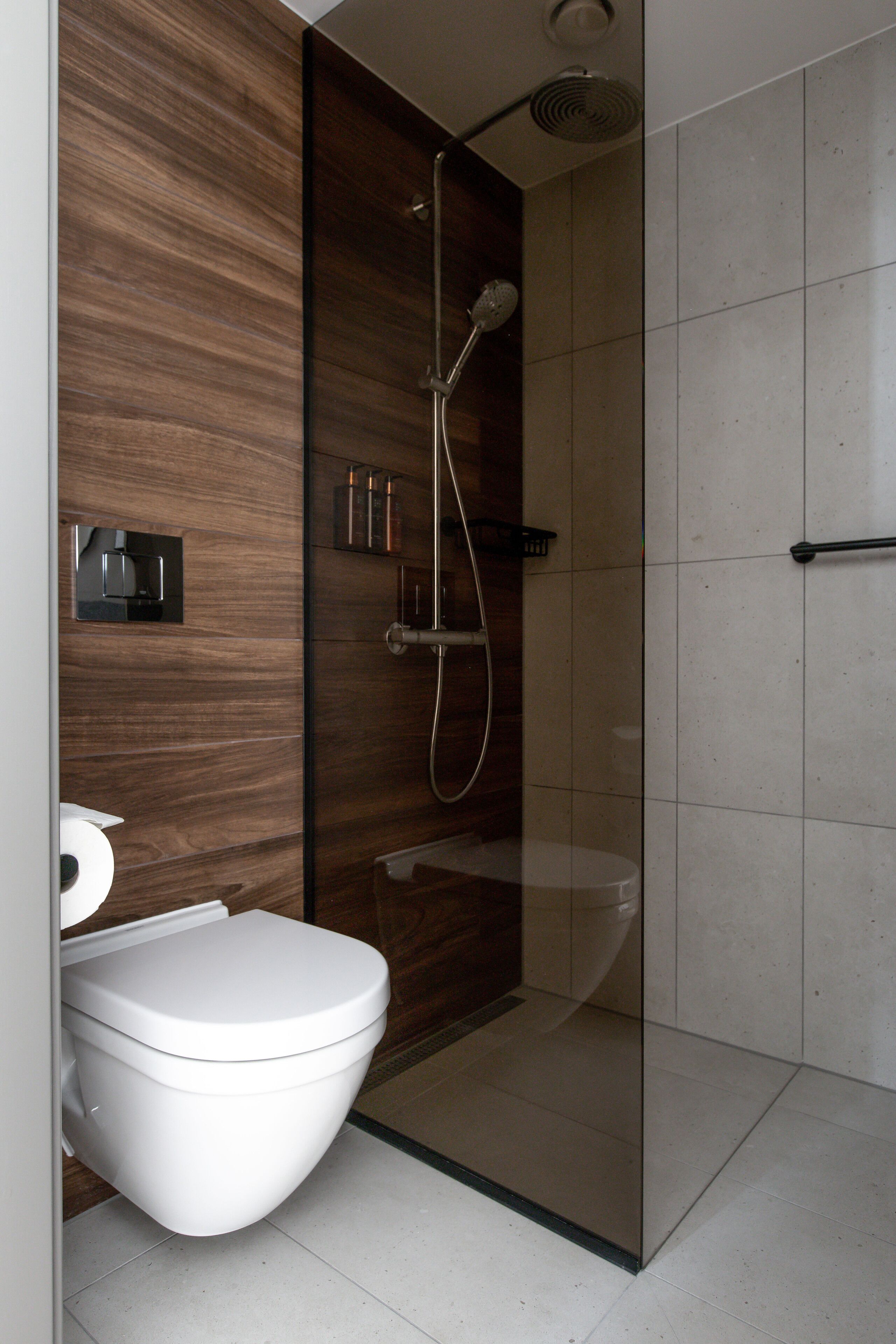Et moderne badeværelse med en glasafskærmet brusekabine, et hvidt toilet og en trækommode.