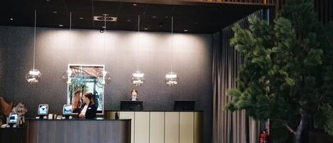 Un área de recepción con diseño moderno, que incluye un mostrador de recepción, un espejo grande y una pared decorativa con listones de madera verticales.
