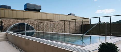 A rooftop swimming pool with a glass enclosure, a brick wall, and a metal railing.