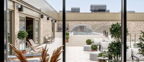 Terraço no telhado com cadeiras de estar, plantas em vasos e área envidraçada.
