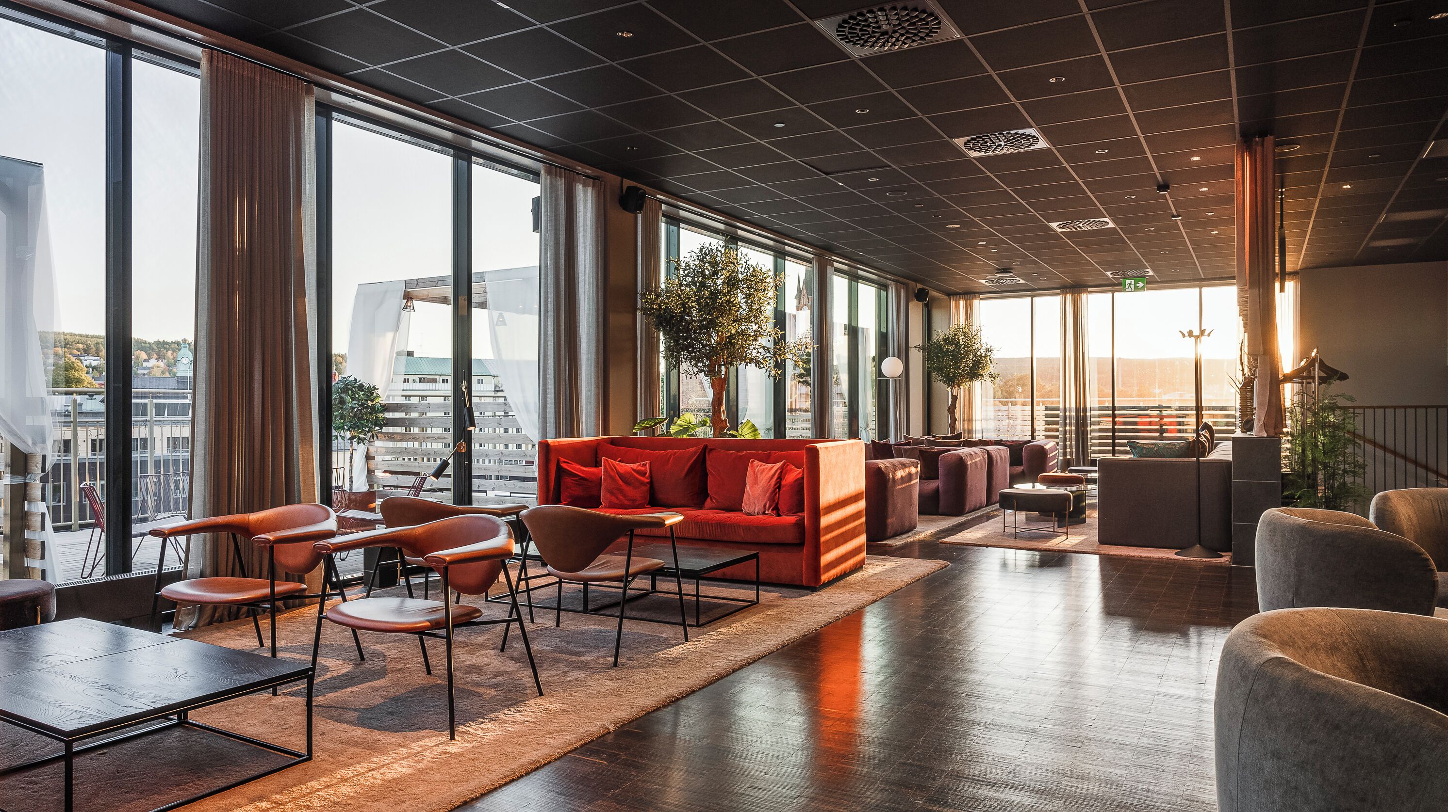 A spacious lounge area with a red sofa, multiple seating options, and large windows offering a city view.