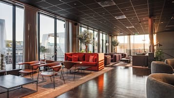 Amplia sala de estar con un sofá rojo, diversas opciones de asientos y grandes ventanales con vista a la ciudad.