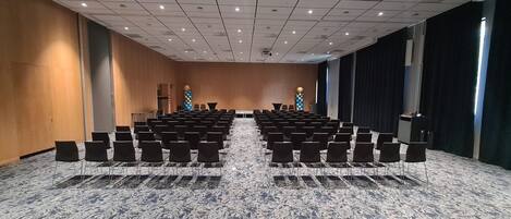 Un salón de conferencias con filas de sillas y un escenario.