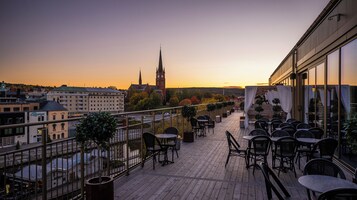 Una terraza en la azotea con mobiliario exterior y vistas a un paisaje urbano que incluye una torre del reloj.