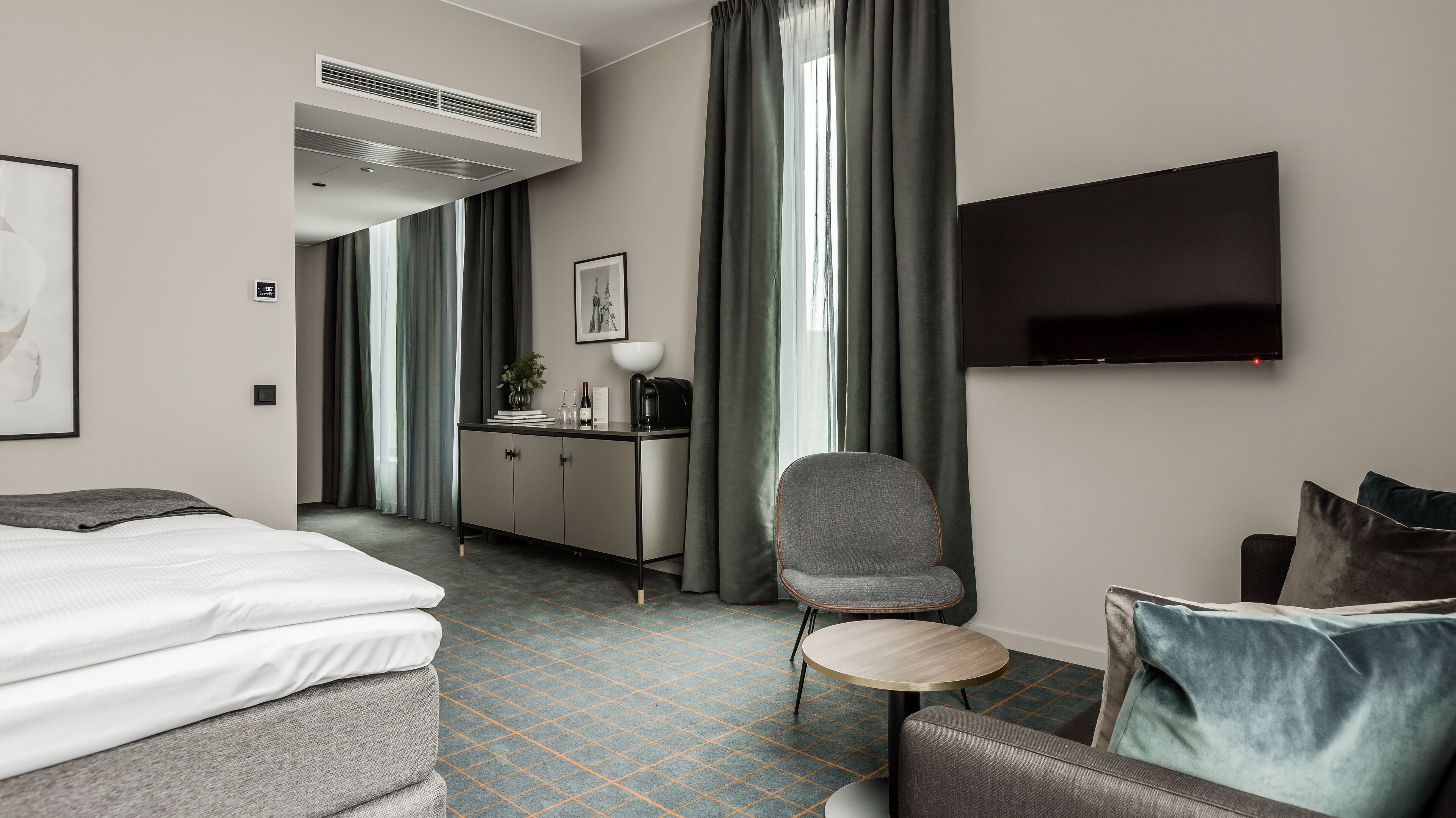 A hotel room with a bed, a desk, a chair, a TV, and a large window with curtains.