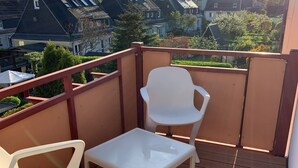 Un balcone con due sedie di plastica bianca e un tavolino, affacciato su una zona residenziale con case e alberi.