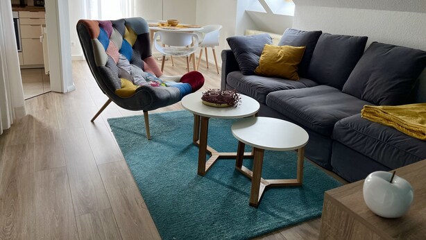 Un soggiorno moderno con un divano grigio, una poltrona colorata, un tavolino rotondo con un oggetto decorativo e, sullo sfondo, un'area da pranzo.