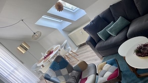 Un soggiorno moderno con un divano scuro, due poltrone con cuscini decorati, un tavolino rotondo e una zona pranzo con tavolo e sedie bianche.