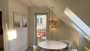 Un'area pranzo moderna con un tavolo rotondo e sedie bianche, un lampadario a sospensione e vista del balcone esterno.