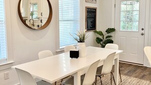 Un espace repas moderne avec une table blanche, quatre chaises, un miroir rond et une plante en pot.